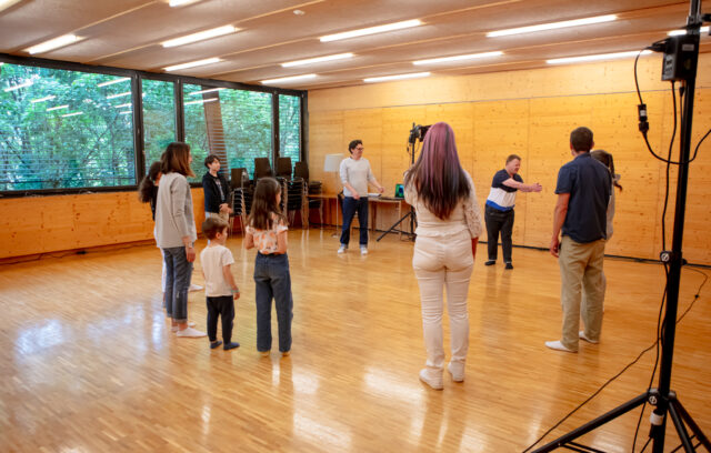 des personnes font du théâtre ensemble. Il y a des adultes et des enfants. Tout le monde a l'air très content.