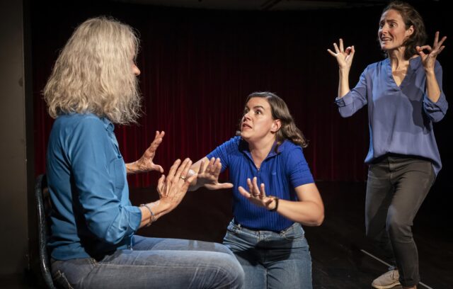 trois comédiennes sont en train de jouer une histoire. Une comédienne est de dos. Les deux autres comédiennes la regardent avec une expression d'affolement.