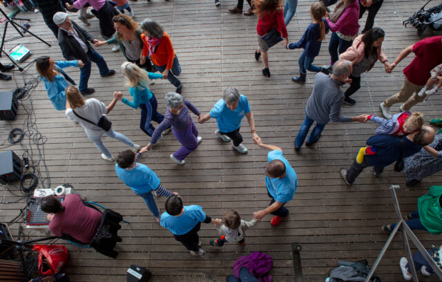 Il y a beaucoup de personnes sur la piste danse. Elles dansent en cercle. Il y a beaucoup de mouvement. Il y a beaucoup de joie.
